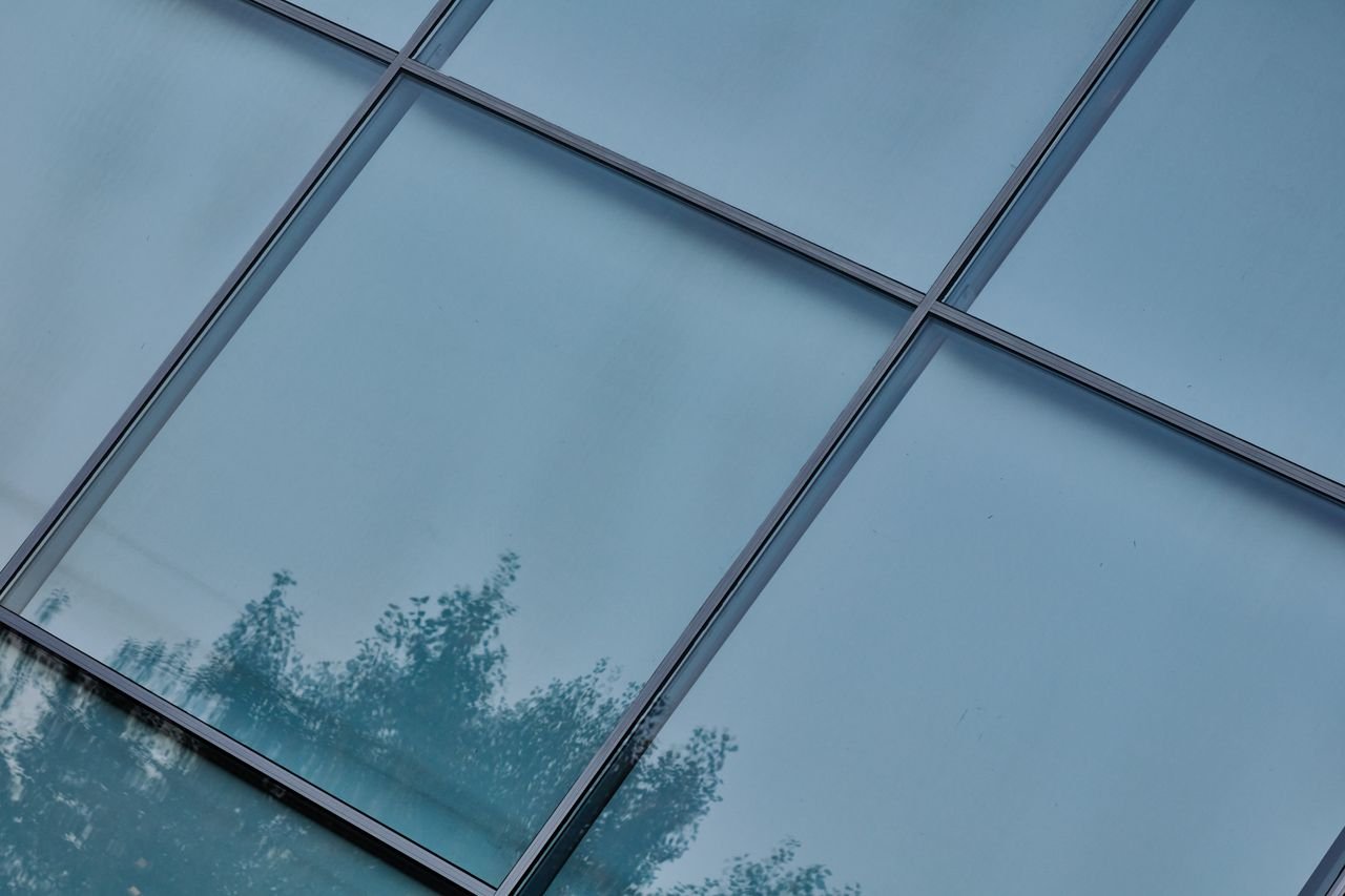 Reflective glass facade of a building with tree silhouettes.